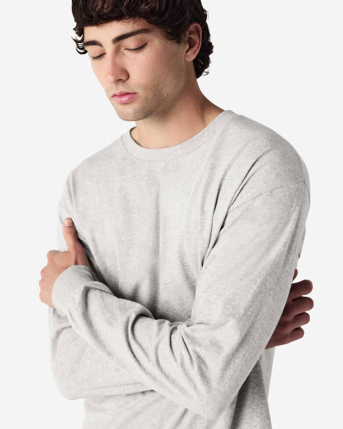 A grey long sleeve T-shirt worn by a model with arms crossed, featuring a visible logo.