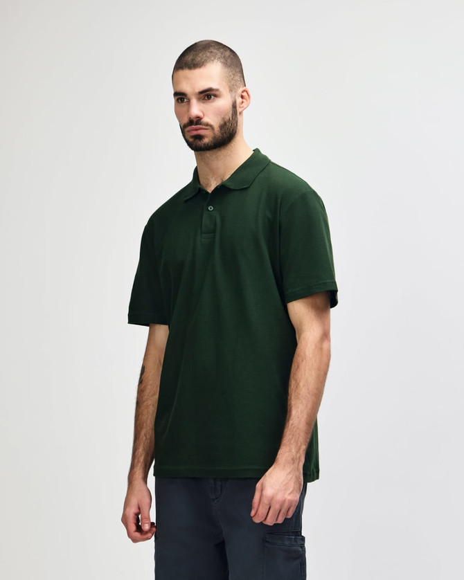 A model wearing a dark green polo shirt with a classic collar and short sleeves, featuring a logo.