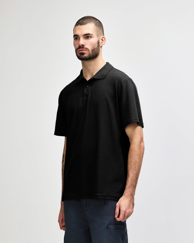 A model wearing a black Gildan Softstyle Adult Double Pique Polo, featuring a classic polo collar and short sleeves.