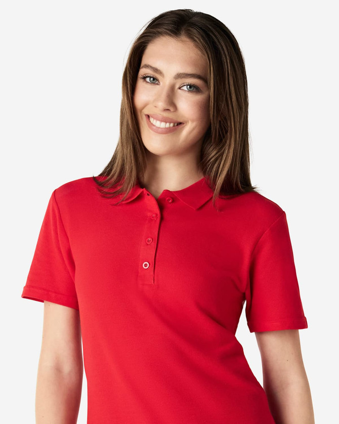A woman is wearing a red Gildan Softstyle ladies' double pique polo, featuring a classic collar and buttons.