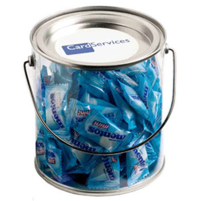 A clear PVC bucket filled with blue-wrapped Mentos mints. The bucket has a metal handle and a logo on top.