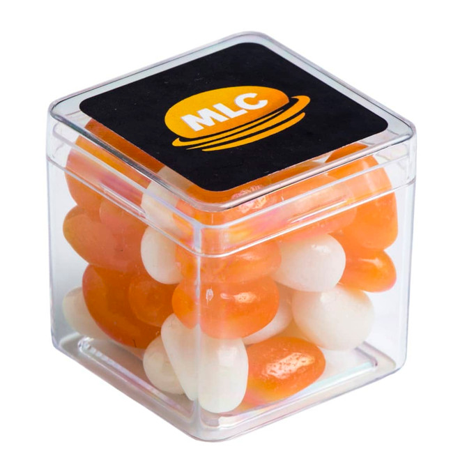 A clear cube container filled with orange and white jelly beans, with a branding logo on the lid.