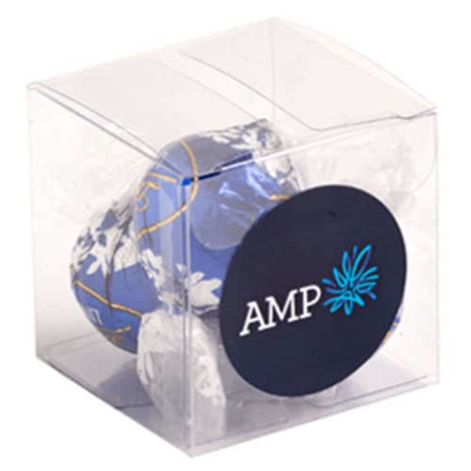A clear cube packaging containing blue and white wrapped chocolate balls. The packaging features a logo.