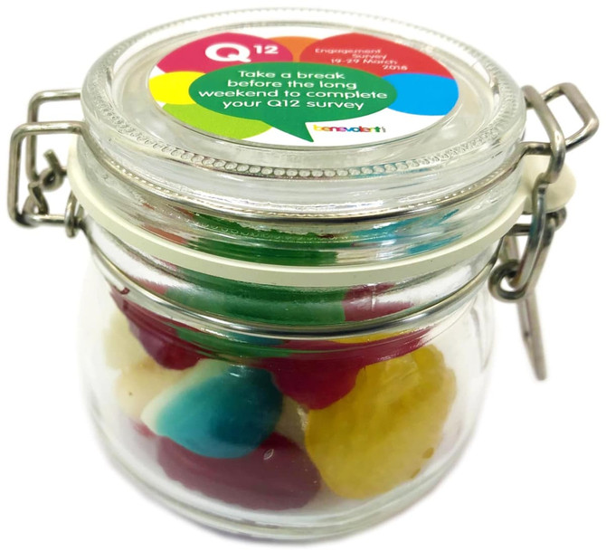 A glass canister filled with mixed lollies in various colours, including red, green, blue, and yellow.