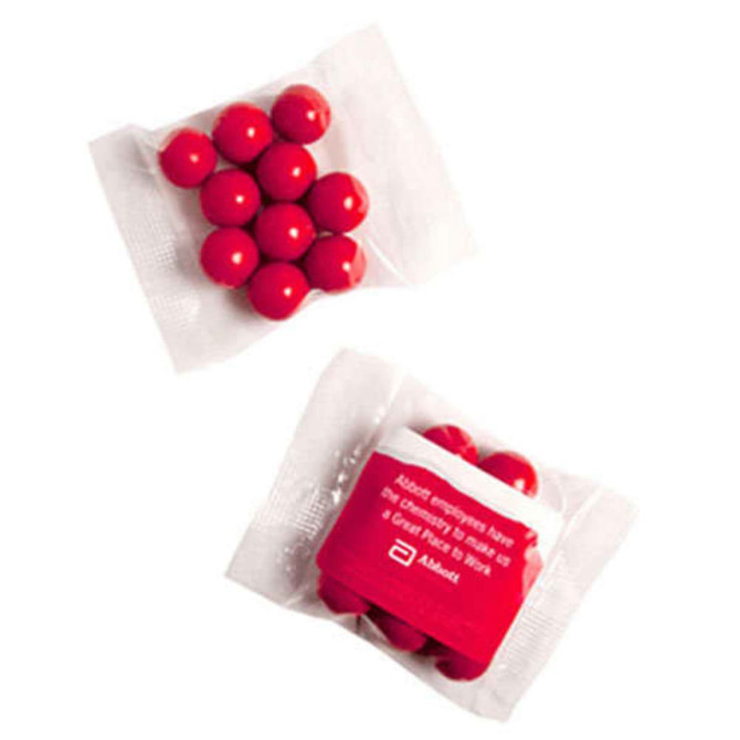 A pack containing round orange chocolate drops, featuring a clear wrapper and a white label with branding.