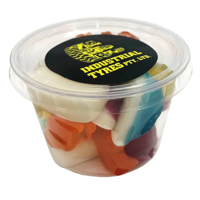 A clear tub filled with mixed lollies in various colours, including red, blue, yellow, and white. It features a logo on the lid.
