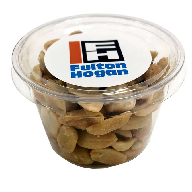 A clear container filled with mixed nuts, featuring light brown and green hues, with a logo on the lid.