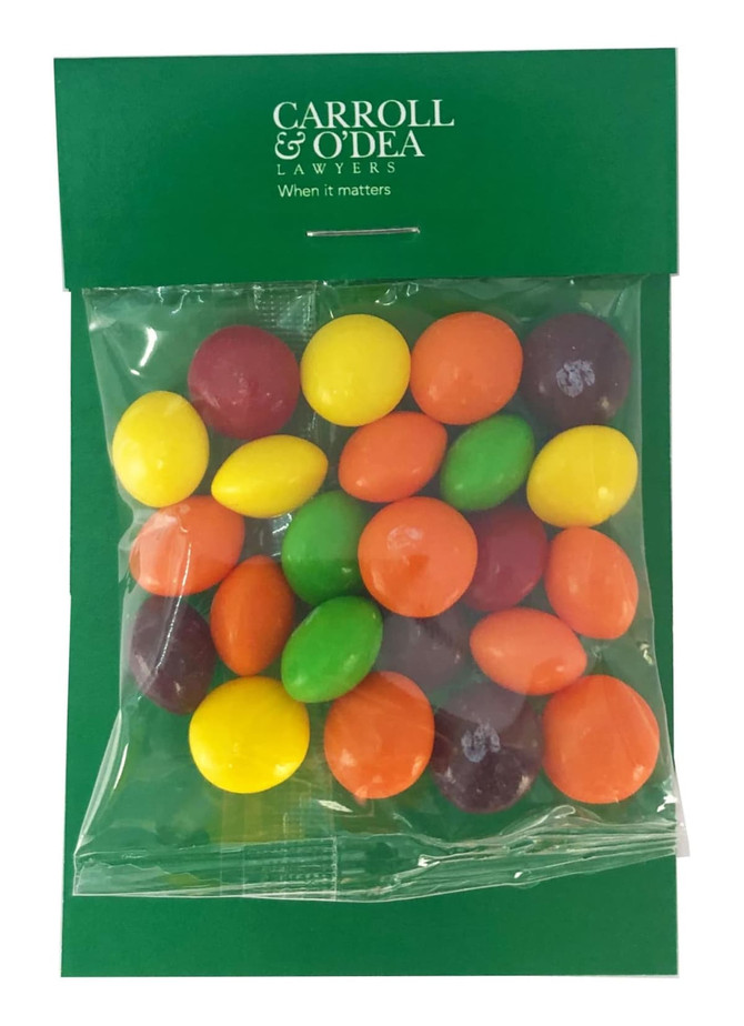 A clear bag containing multicoloured Skittles in yellow, green, red, purple, and orange hues, with a branded header.