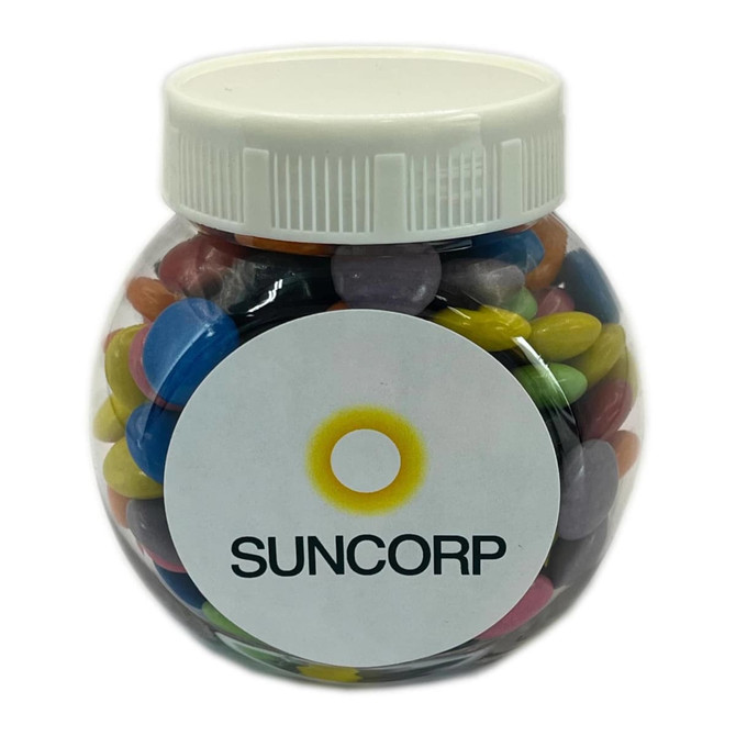 A clear plastic jar filled with colourful choc beans, featuring a white lid and a label with a logo.