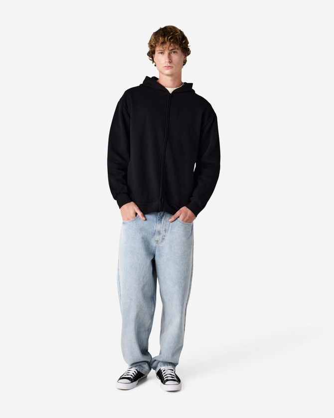A model wearing a black unisex full zip hooded sweatshirt paired with light blue baggy jeans and black sneakers.