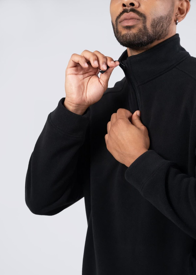 A man in a black polar fleece half zip top, adjusting the zip at the collar. The top features a logo.
