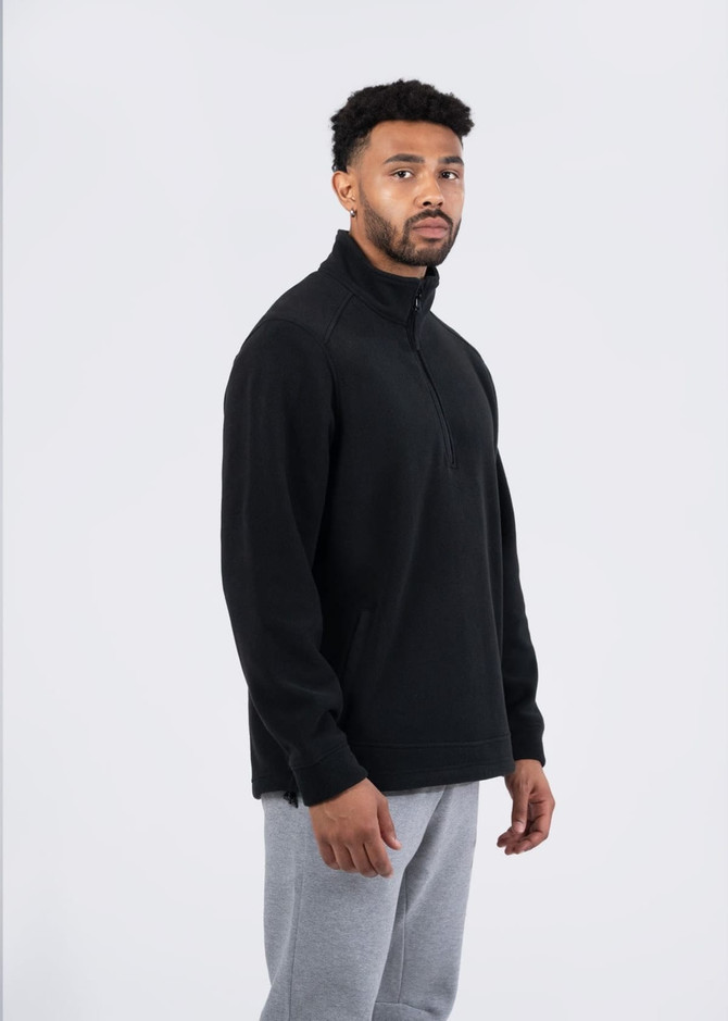 A black polar fleece half zip top worn by a male model, styled with grey pants, featuring a logo.