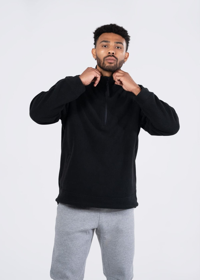 A black polar fleece half zip top being worn by a model, paired with grey pants. The jacket features a logo.