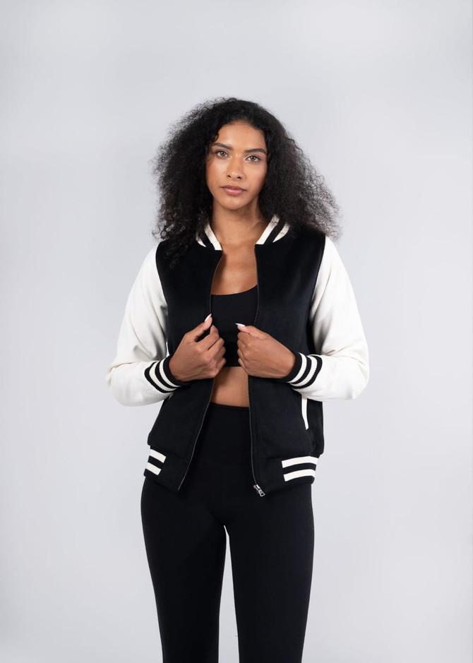 A black and white women's varsity jacket made from a soft wool blend, featuring a logo and striped detailing.
