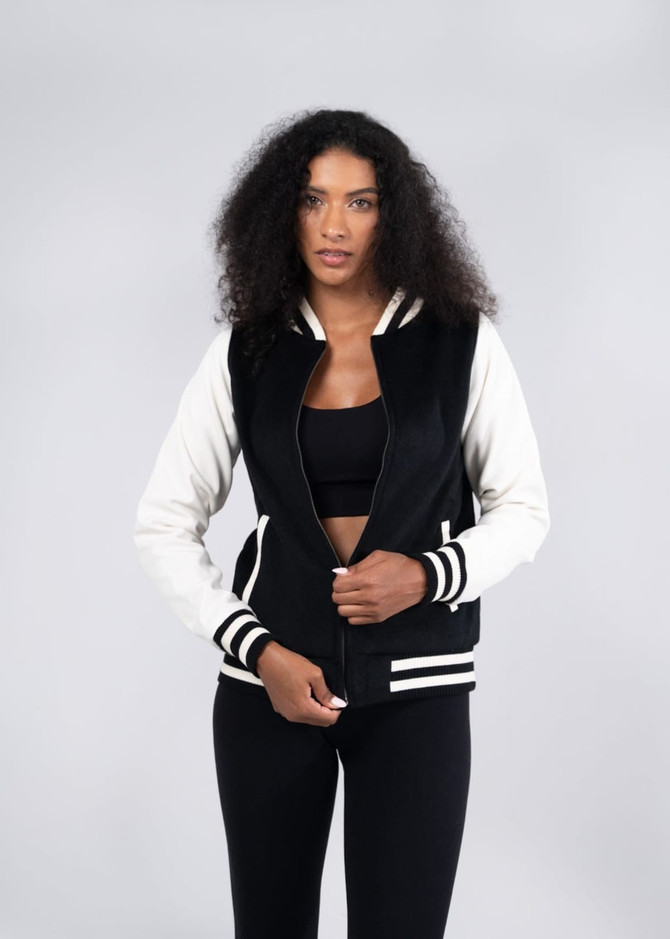 A black and cream varsity jacket with a soft shell finish, featuring striped ribbed cuffs and a logo.