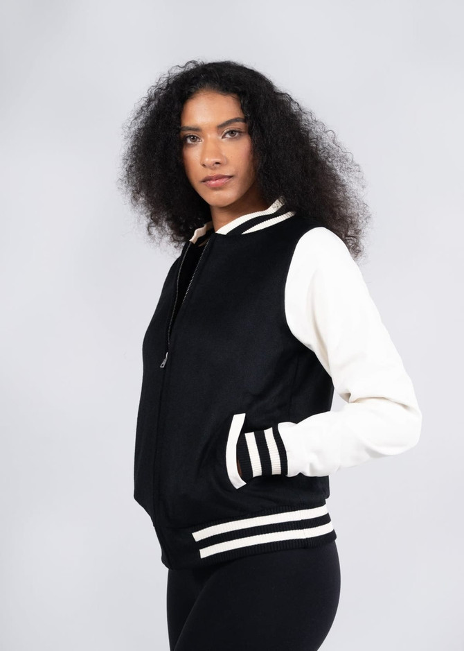 A black and white wool blend soft shell varsity jacket with striped cuffs, worn by a model. The jacket features a logo.