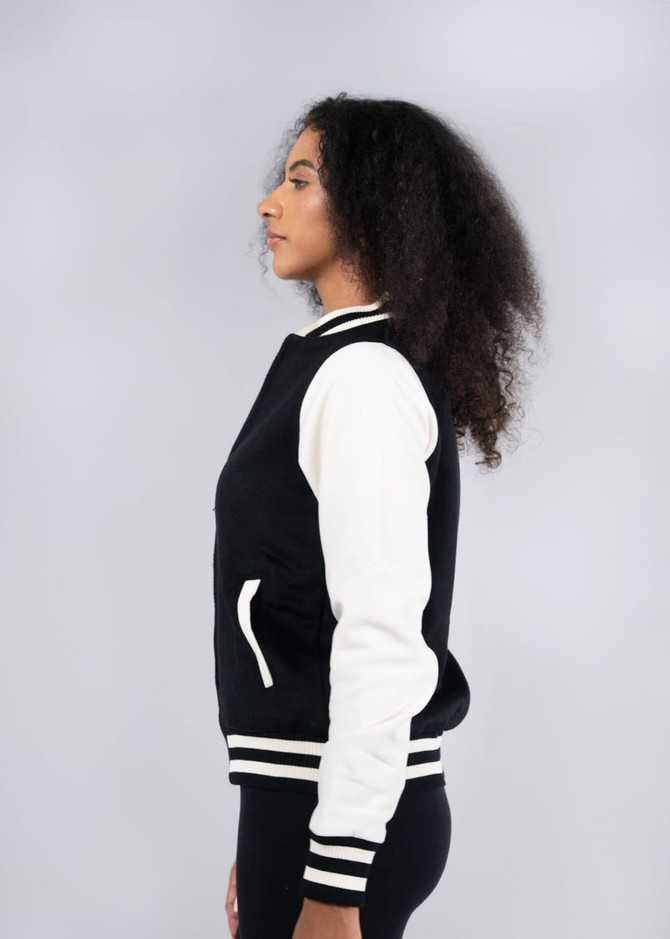 A black and white women's varsity jacket with a logo, shown from the side, featuring a soft shell design.