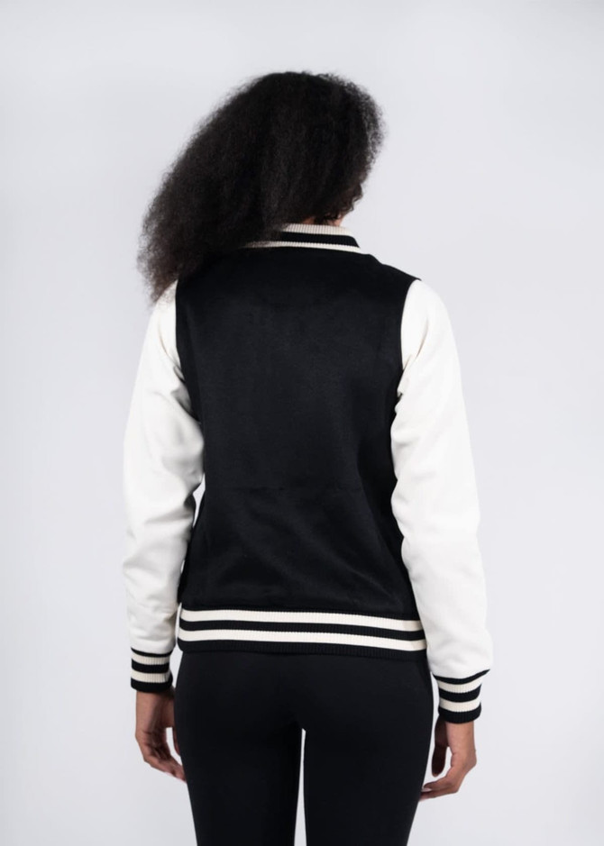 A black and white women's varsity jacket with a soft shell design, featuring a logo on the back.