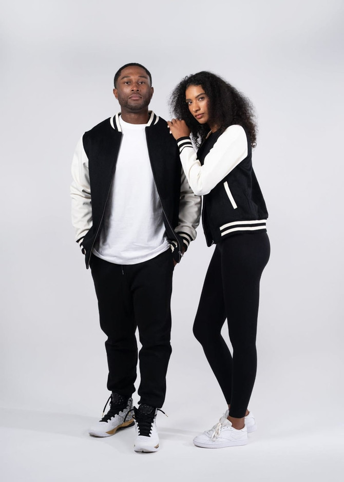 A black and white wool blend varsity jacket worn by a man and a woman, featuring a logo. Both models are in casual attire.
