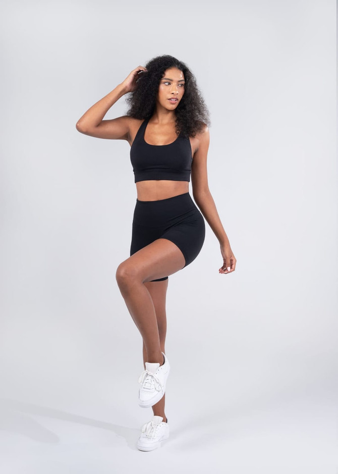 A model poses in black high rise legging shorts paired with a matching sports bra and white sneakers.