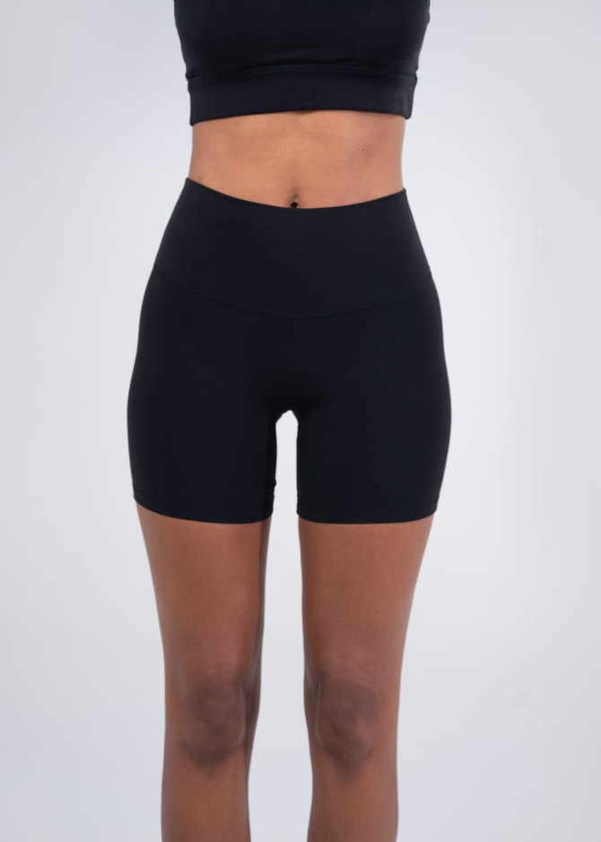High-rise black legging shorts on a model, paired with grey sneakers. Features a brand logo on the waistband.