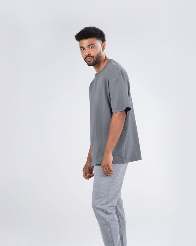 A grey unisex oversize easyfit tee worn by a man, paired with light grey pants, against a plain background.