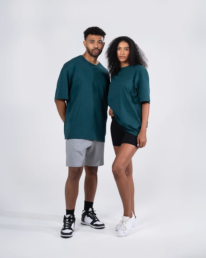 Two models wearing unisex oversize easy-fit tees in teal, paired with shorts and stylish sneakers.