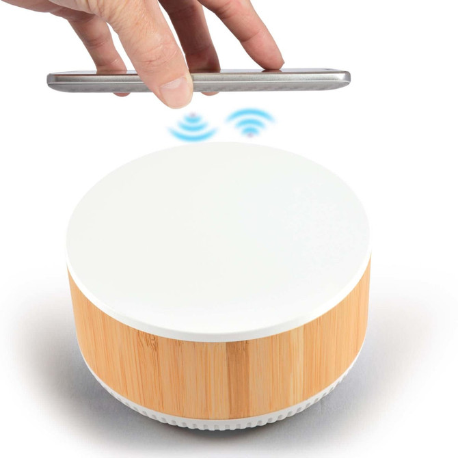 A wireless charger and speaker with a white top and bamboo base, featuring a hand holding a smartphone above it.