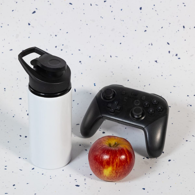 A drink bottle in white with a black free flow lid, placed alongside a red apple and a black game controller.