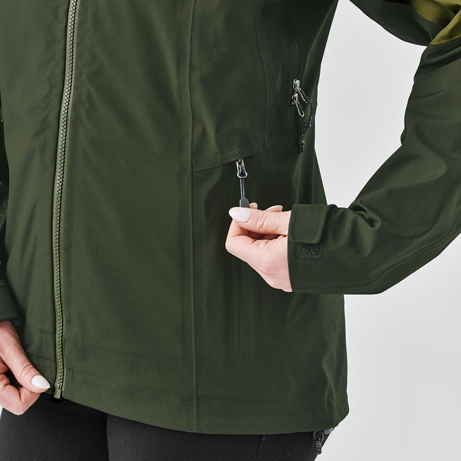A green women's jacket with zipped pockets, featuring a high collar and a snug fit. It has a logo on the arm.