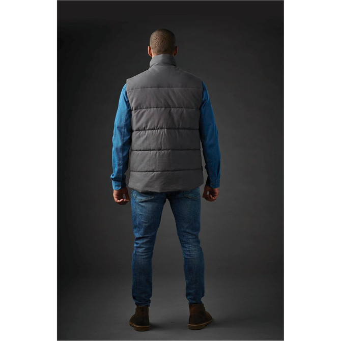 A man wearing a grey thermal vest stands with his back to the camera, paired with a blue shirt and jeans.