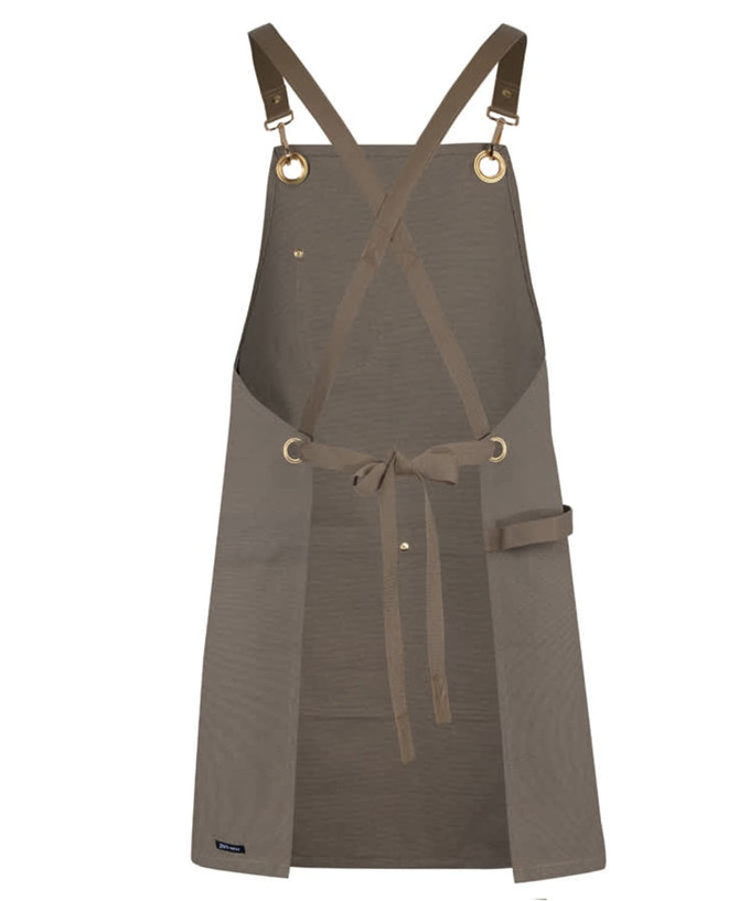 A brown canvas apron featuring brass eyelets and a PU strap, with a waist tie and a side pocket.