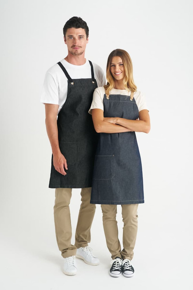 A pair of denim bib aprons in dark blue, worn by a man and a woman, featuring adjustable straps and pockets.