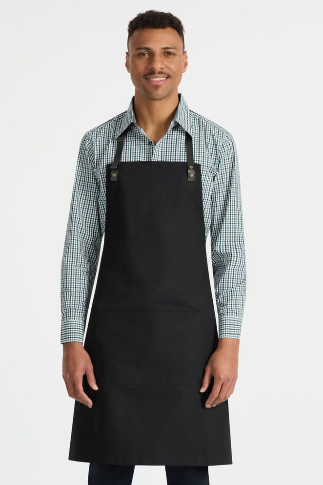 A black bib apron with adjustable straps, featuring a front pocket, worn by a model in a checkered shirt.