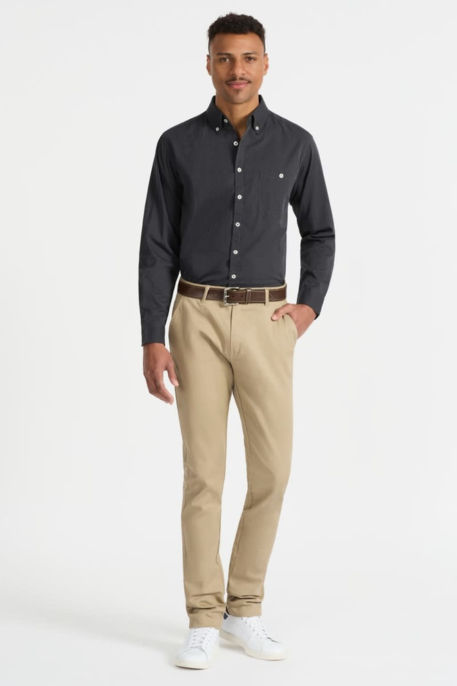 A model wearing a black long sleeve button-up shirt paired with beige trousers and white shoes, featuring a small logo.