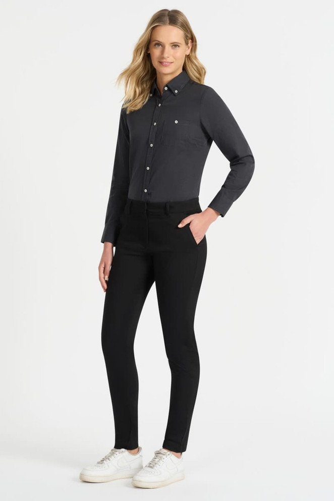 A woman wearing a black chino pant paired with a dark shirt and white sneakers. The outfit features a logo.