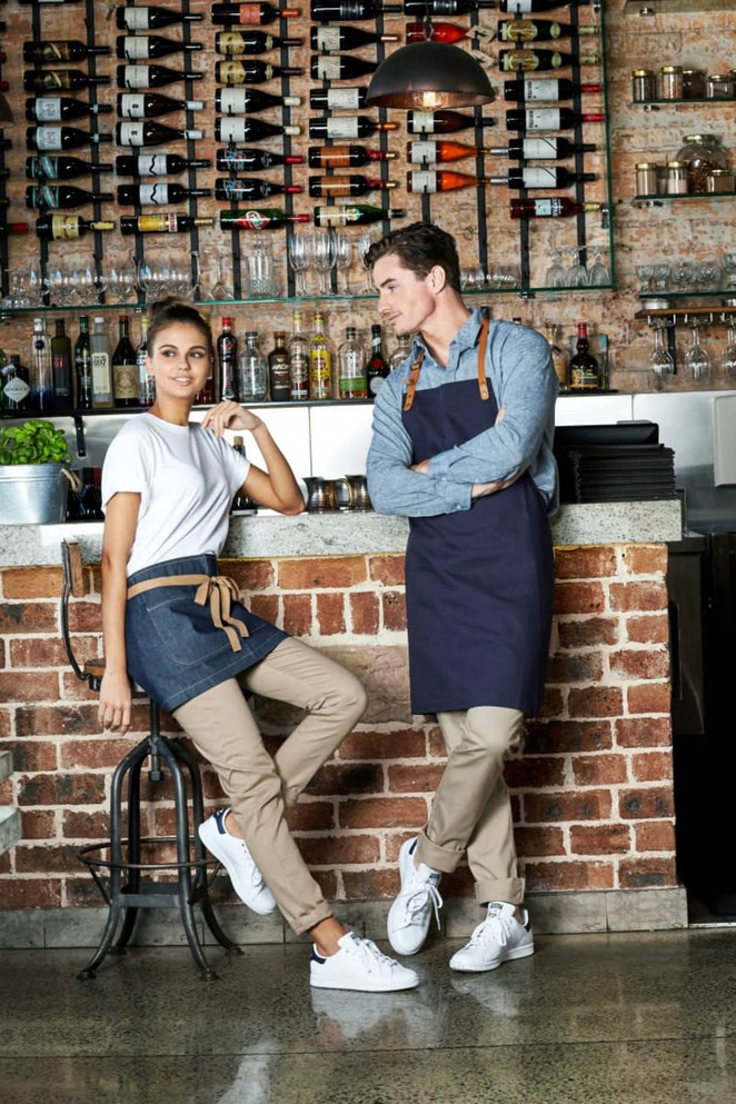 A pair of men's chino pants in a light beige colour, styled with a grey button-up shirt and white sneakers.