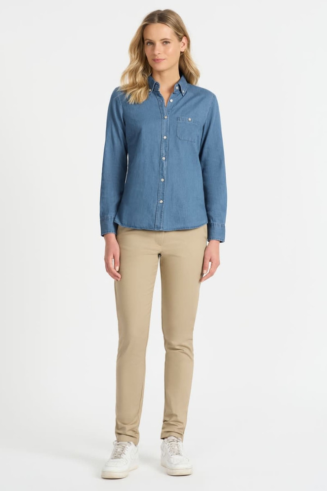A ladies' long sleeve button-up shirt in denim blue, paired with beige trousers and white sneakers. The shirt has a chest pocket and branding.