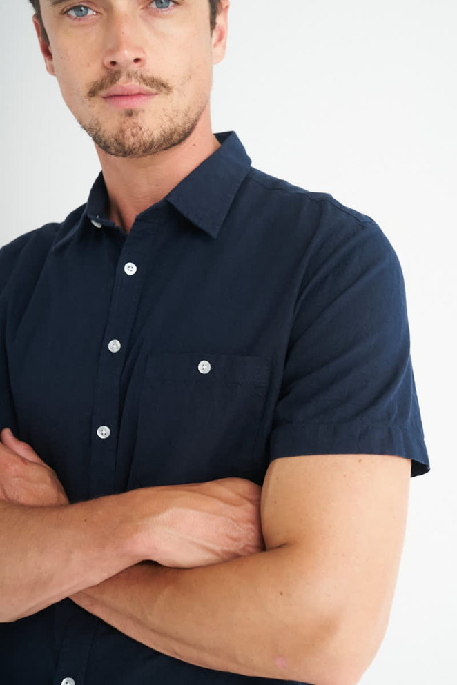 A navy blue short sleeve button-up shirt featuring a chest pocket and white buttons.
