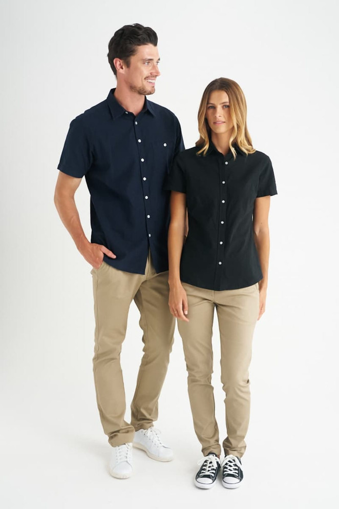 A black ladies short sleeve shirt is displayed on a model, paired with beige pants and sneakers, featuring a logo.