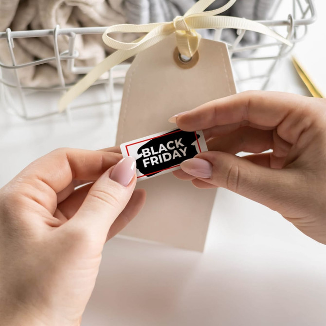 A person holds a small, rectangular sticker with a black and white design, near a tag and a basket of clothing.