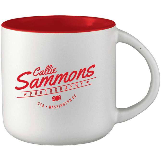 A ceramic mug with a white exterior and red interior, featuring a logo on the side.