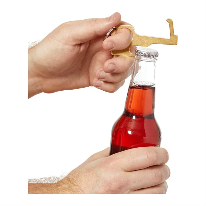A gold No Contact Keychain is being used to open a drink bottle, featuring a rounded handle and a bottle opener tip.
