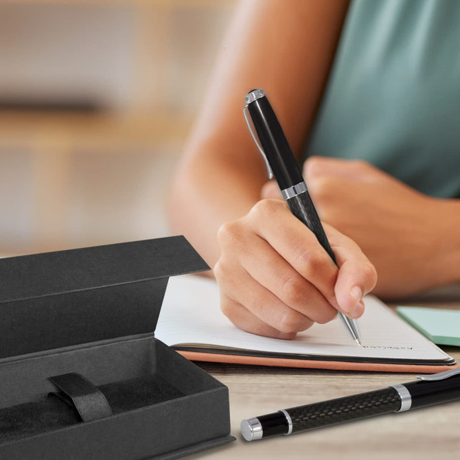 A black pen and a gift box are displayed on a desk while someone writes in a notebook.
