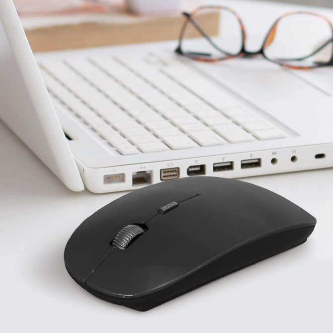 A black travel mouse rests on a desk, next to a white laptop and a pair of glasses. The scene is well-lit and modern.
