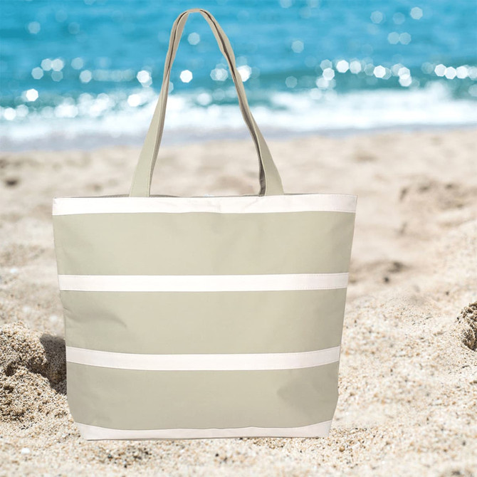 An insulated cooler bag in light grey with white stripes, set against a beach background.
