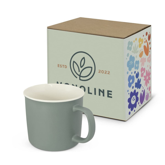 A green coffee mug next to a decorative box featuring floral designs and a logo. The mug has a white interior.