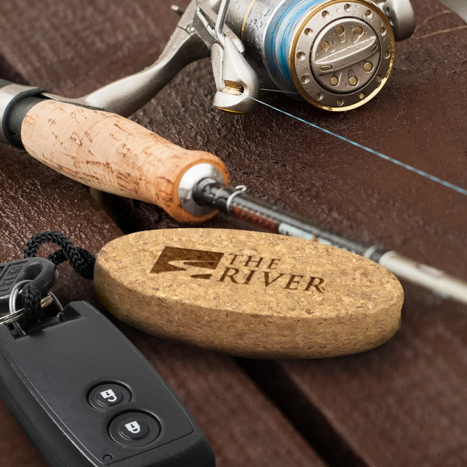 A cork floating key ring in a light brown shade, positioned next to a fishing rod and reel on a wooden surface.