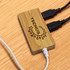A bamboo USB hub with two black cables plugged in, placed on a wooden surface. The hub has a logo.