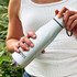 A drink bottle in white, featuring a tapered shape and a black lid, held by a person against a natural background.